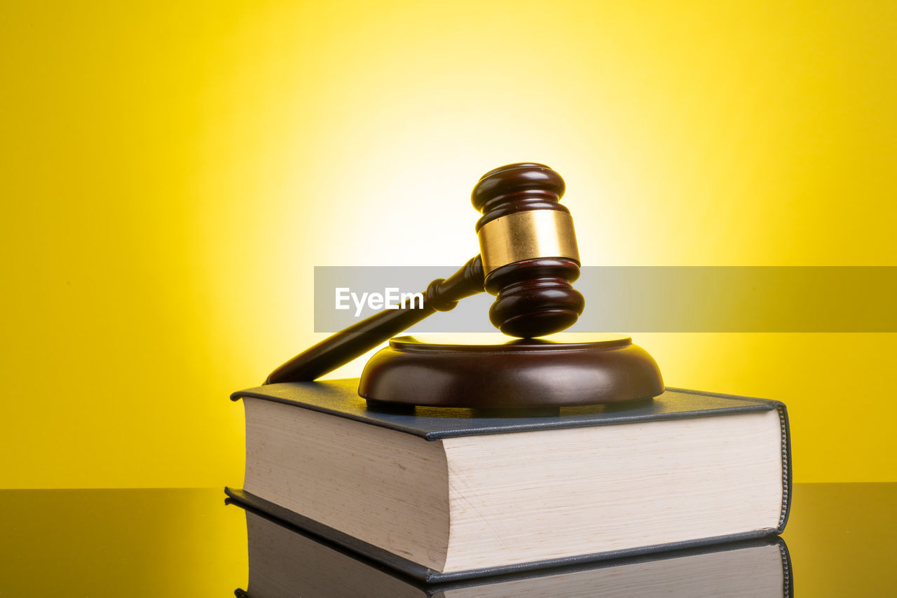 Gavel and book on table against yellow background