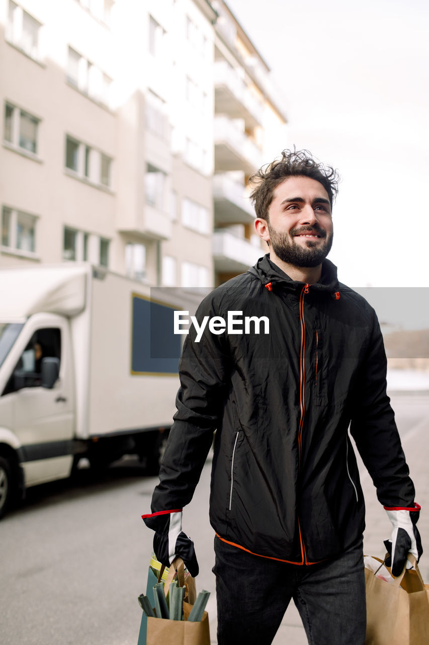 Confident young delivery man carrying grocery bags in city