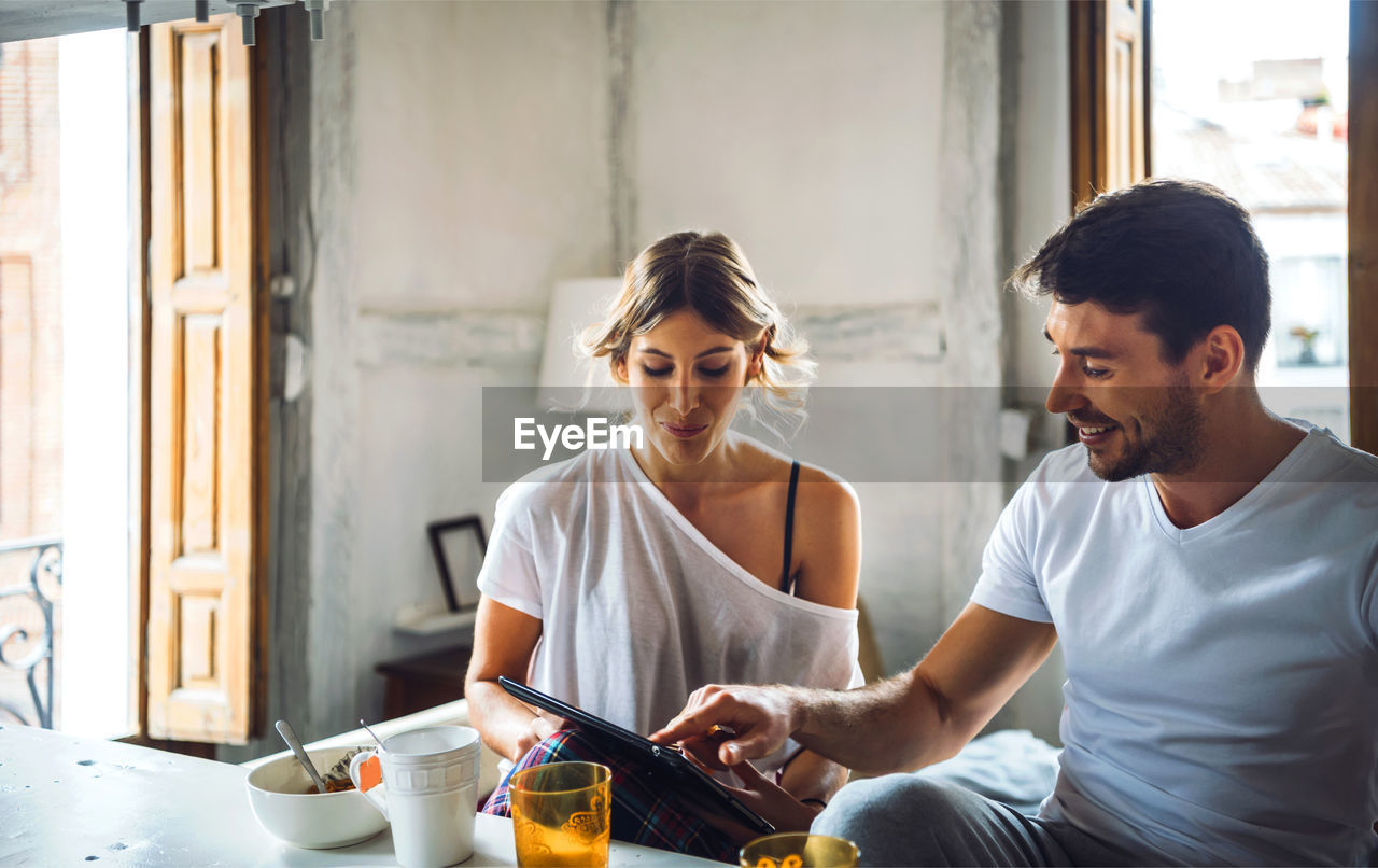 Young couple watching tablet while having breakfast at home