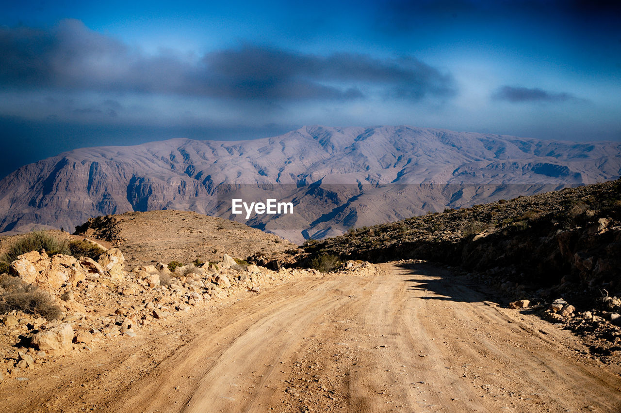 Dirt road amidst mountains against sky