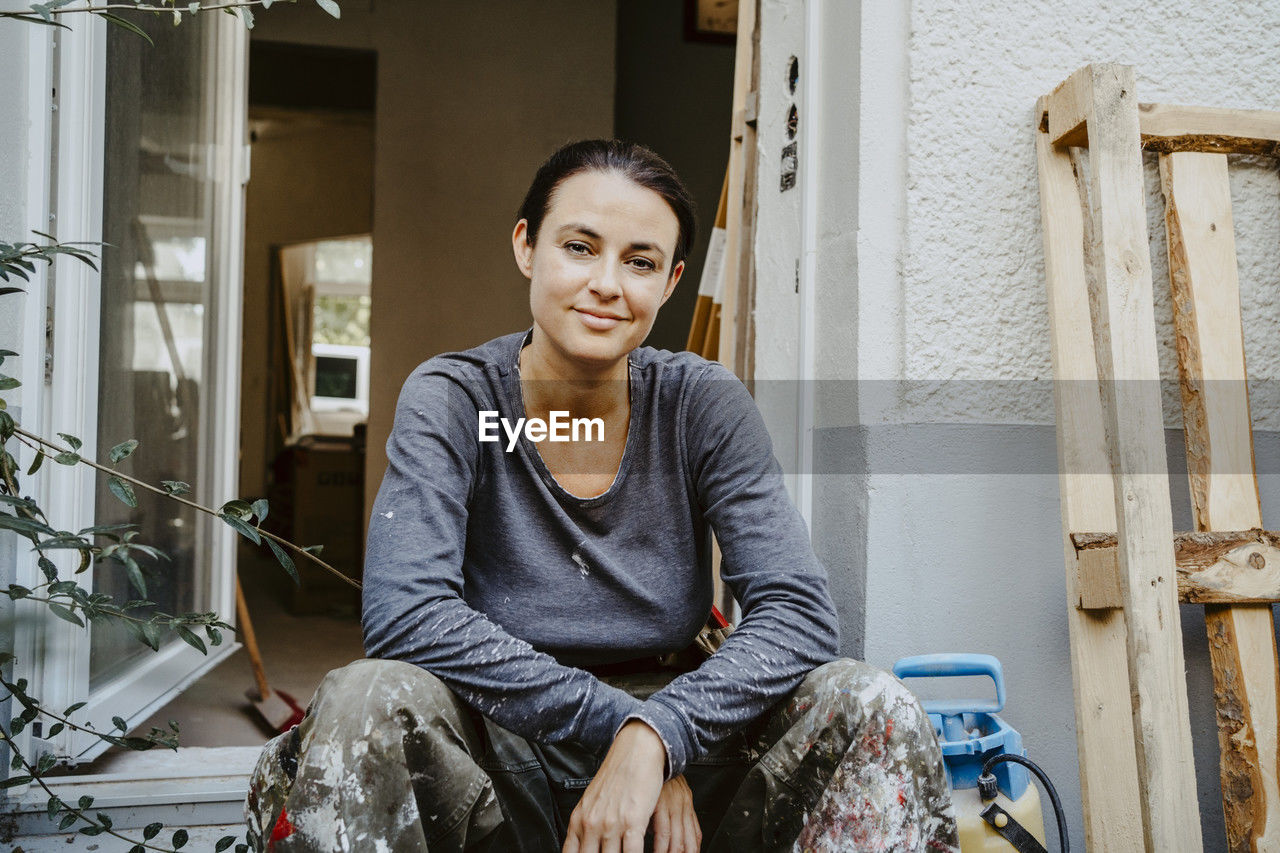 Portrait of smiling female carpenter sitting in front of house entrance