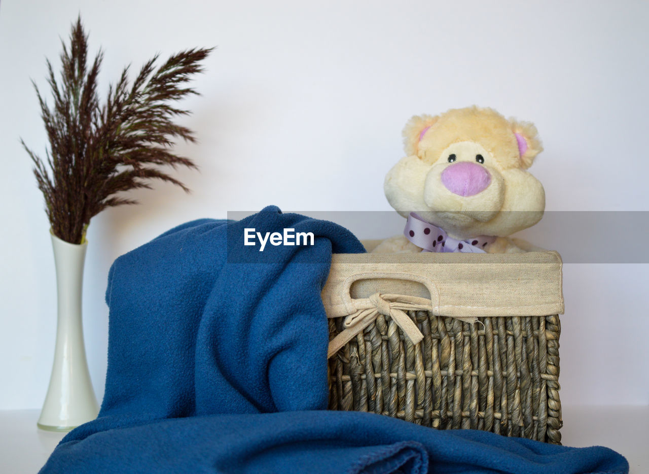 CLOSE-UP OF STUFFED TOY IN BASKET ON TABLE AGAINST WALL