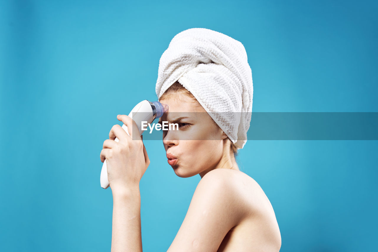 Young woman massaging face against blue background