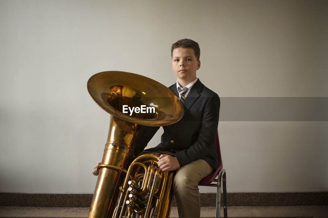 Portrait of confident boy with tuba against white wall