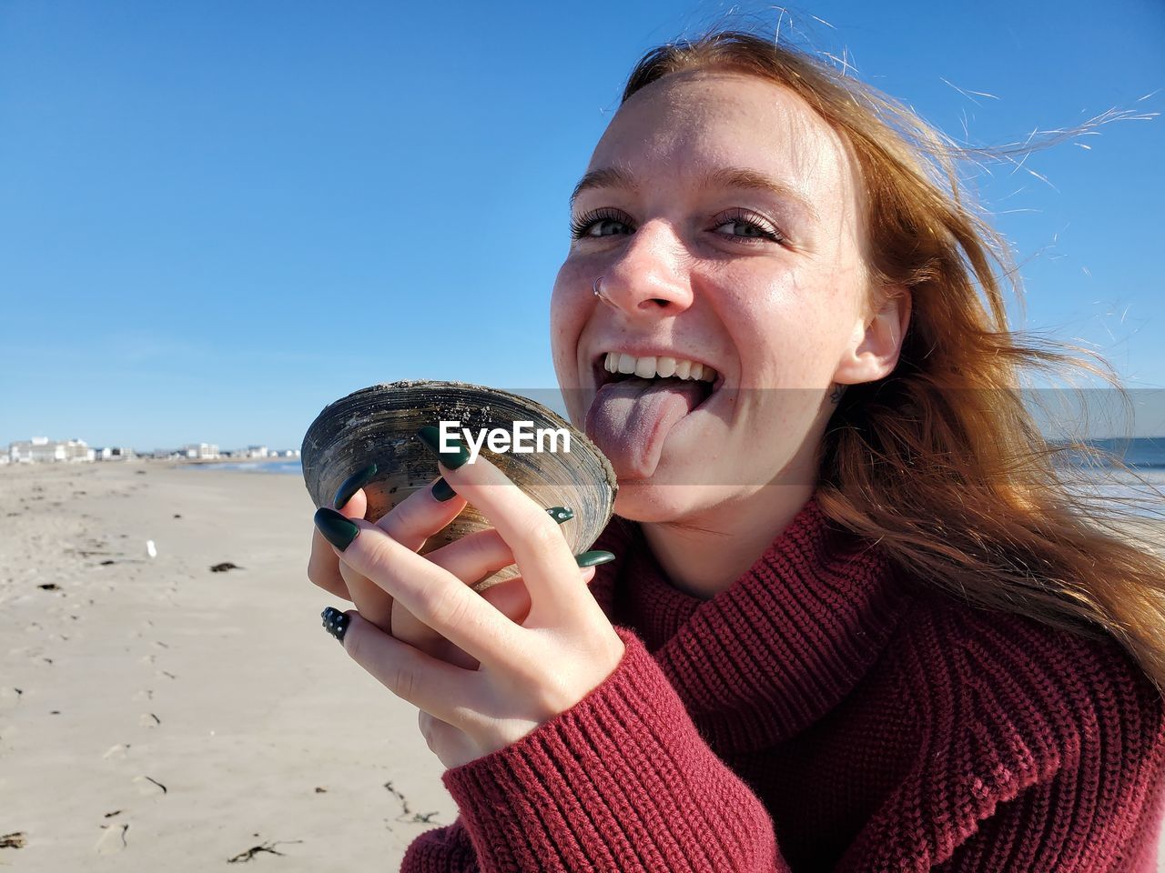 Portrait of smiling woman holding seashell against sky