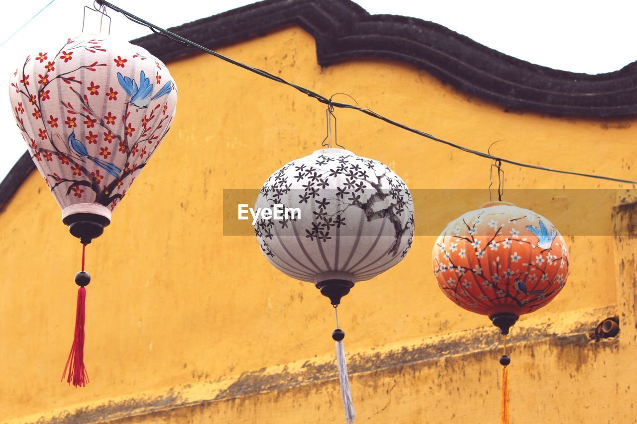 Low angle view of lanterns hanging on cable by building