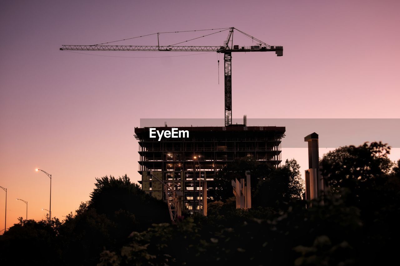 LOW ANGLE VIEW OF CRANE BY SILHOUETTE BUILDING AGAINST SKY