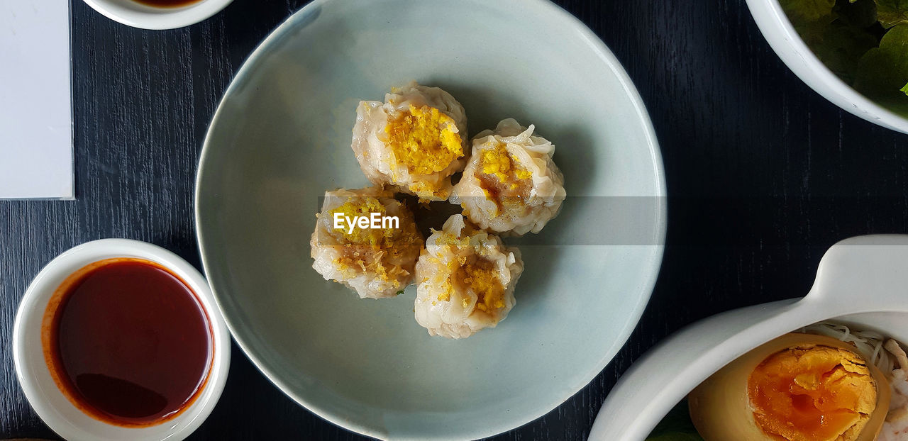 Top view of four steamed dumplings on green dish with sliced boiled egg and sweet sauce.