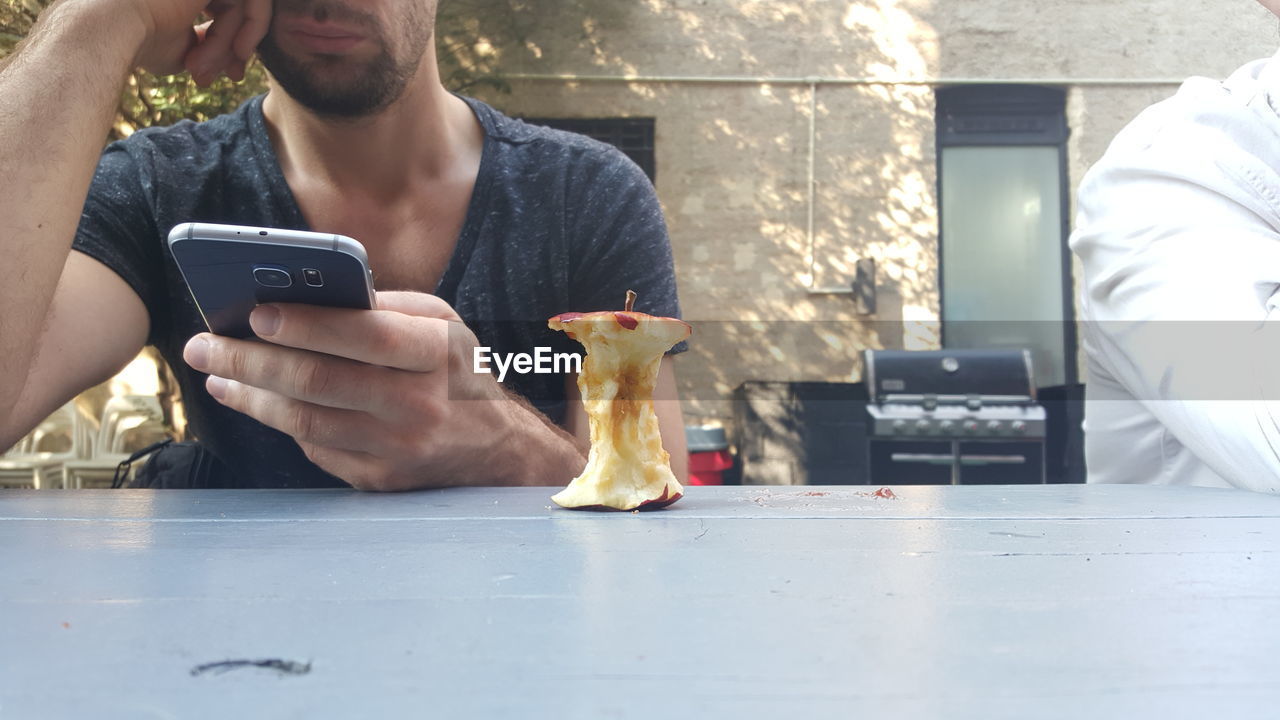 Midsection of man using mobile phone while sitting at table