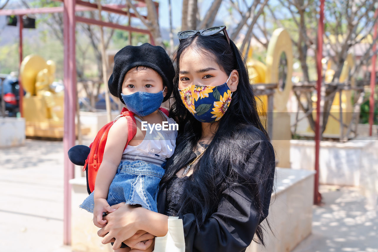 Little child girl and asian mother wearing medical protective mask and holding her daughter 