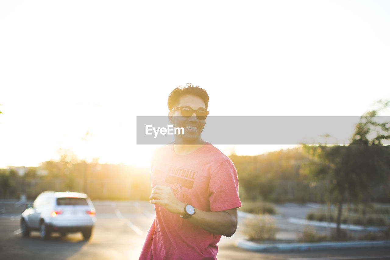 Man in sunglasses standing in parking lot against clear sky during sunset