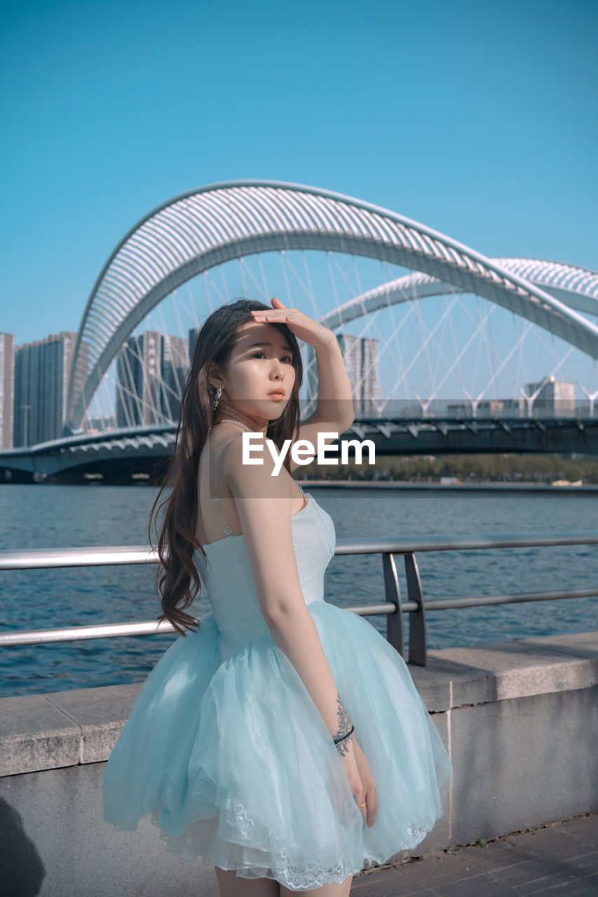 portrait of young woman standing by river against clear sky