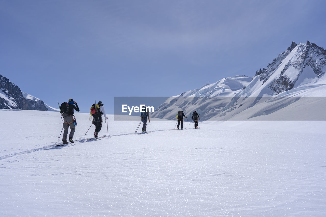Full length of ski mountaineers walking on snowcapped mountain against sky