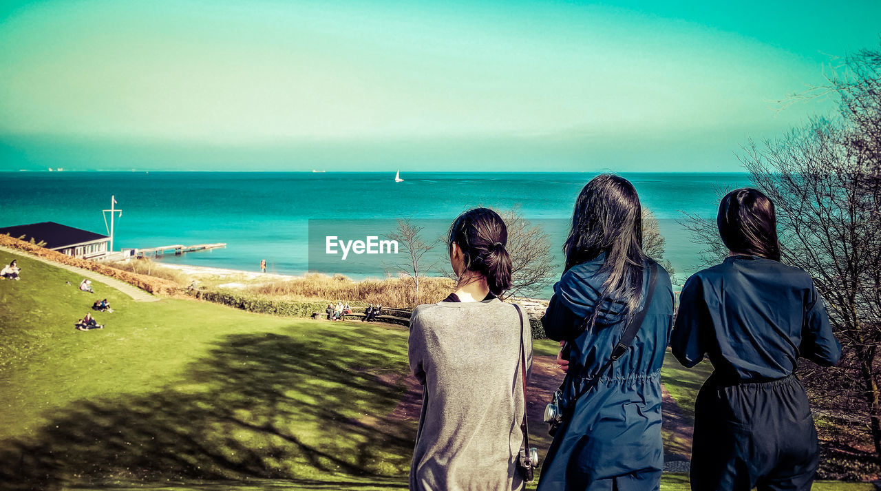 REAR VIEW OF PEOPLE AT BEACH AGAINST SKY