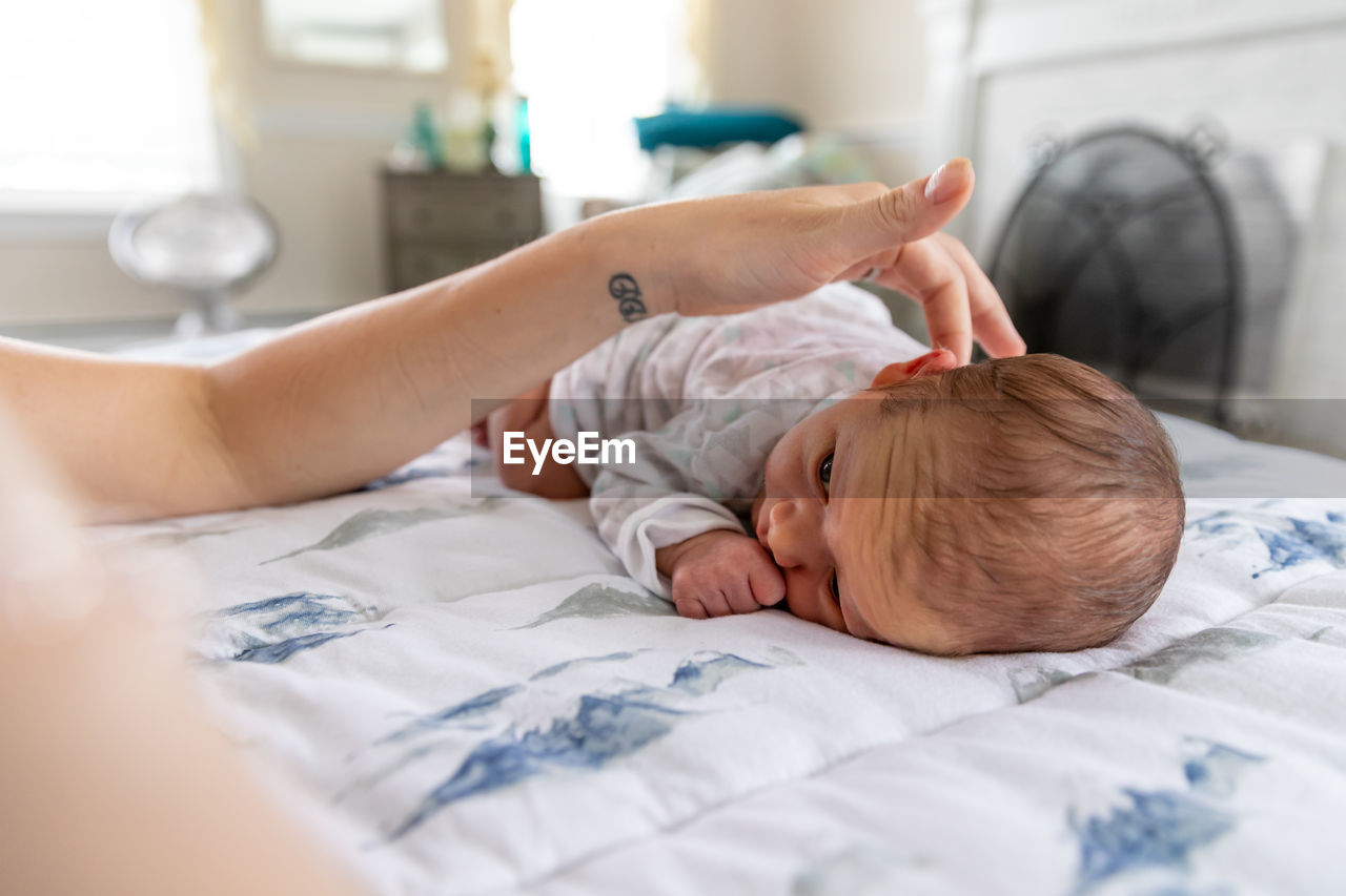 Loving mother gently touching newborn baby laying on stomach.