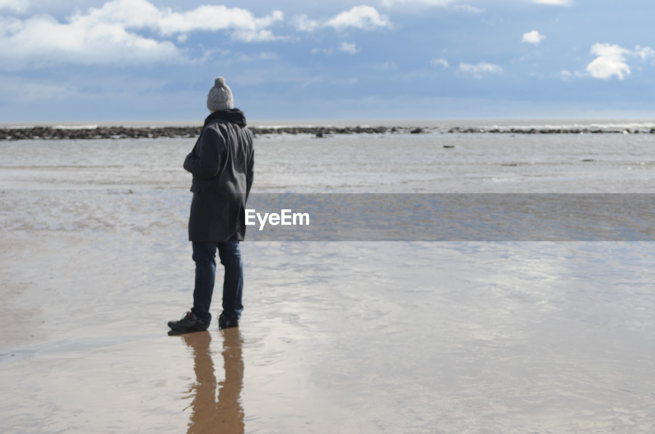 Rear view of person standing on shore at beach against sky