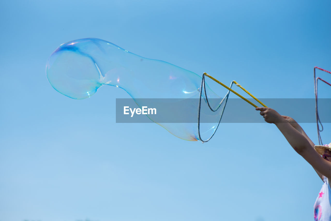 Girl holding bubble wand against clear blue sky