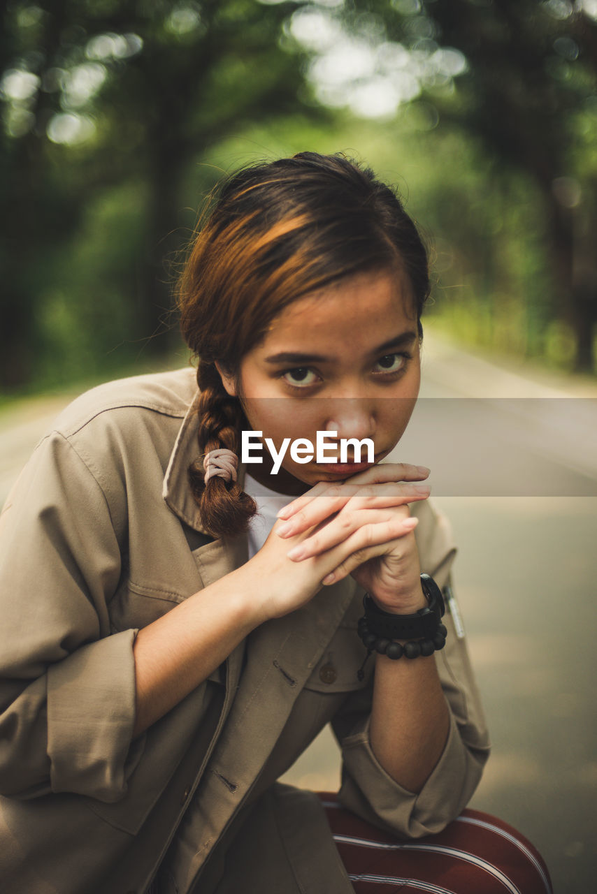 Portrait of young woman with hands clasped sitting on road