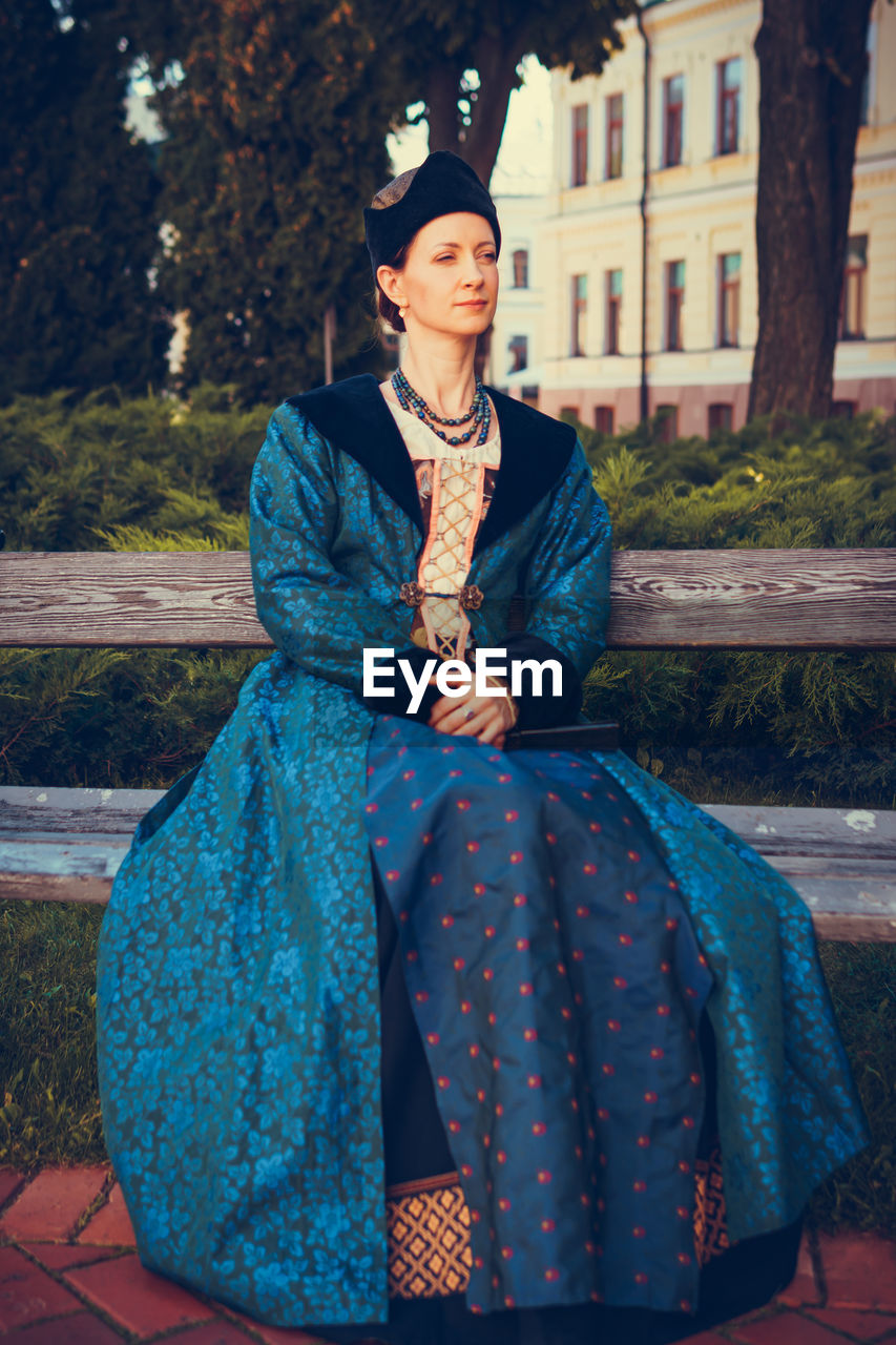 PORTRAIT OF WOMAN SITTING ON BENCH AGAINST OUTDOORS