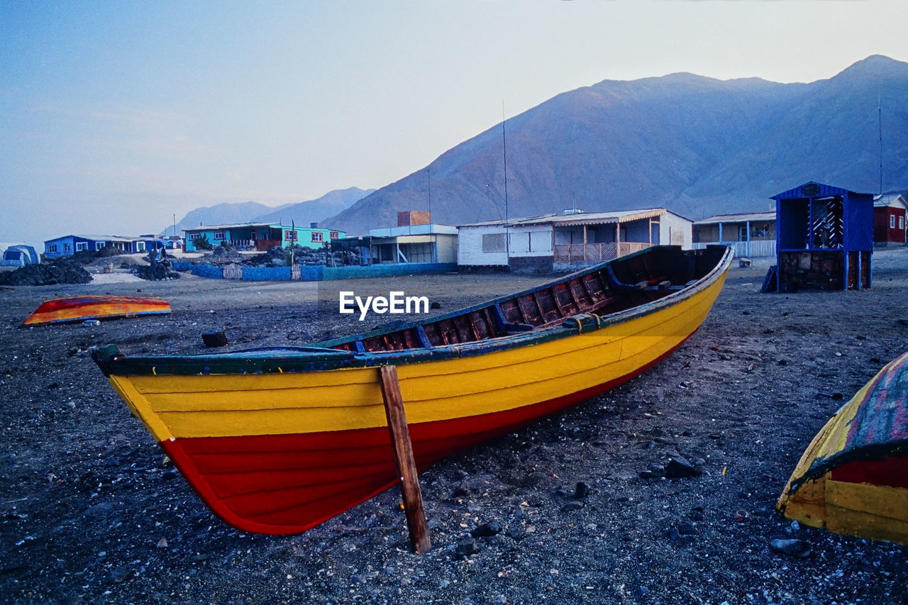 Boats moored on sea by mountain against sky