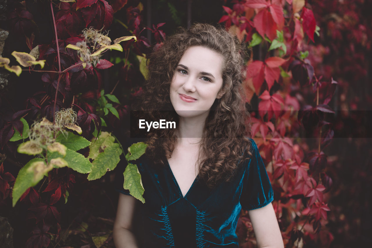 Beautiful curly hair young woman in dark blue velvet dress in an autumn park