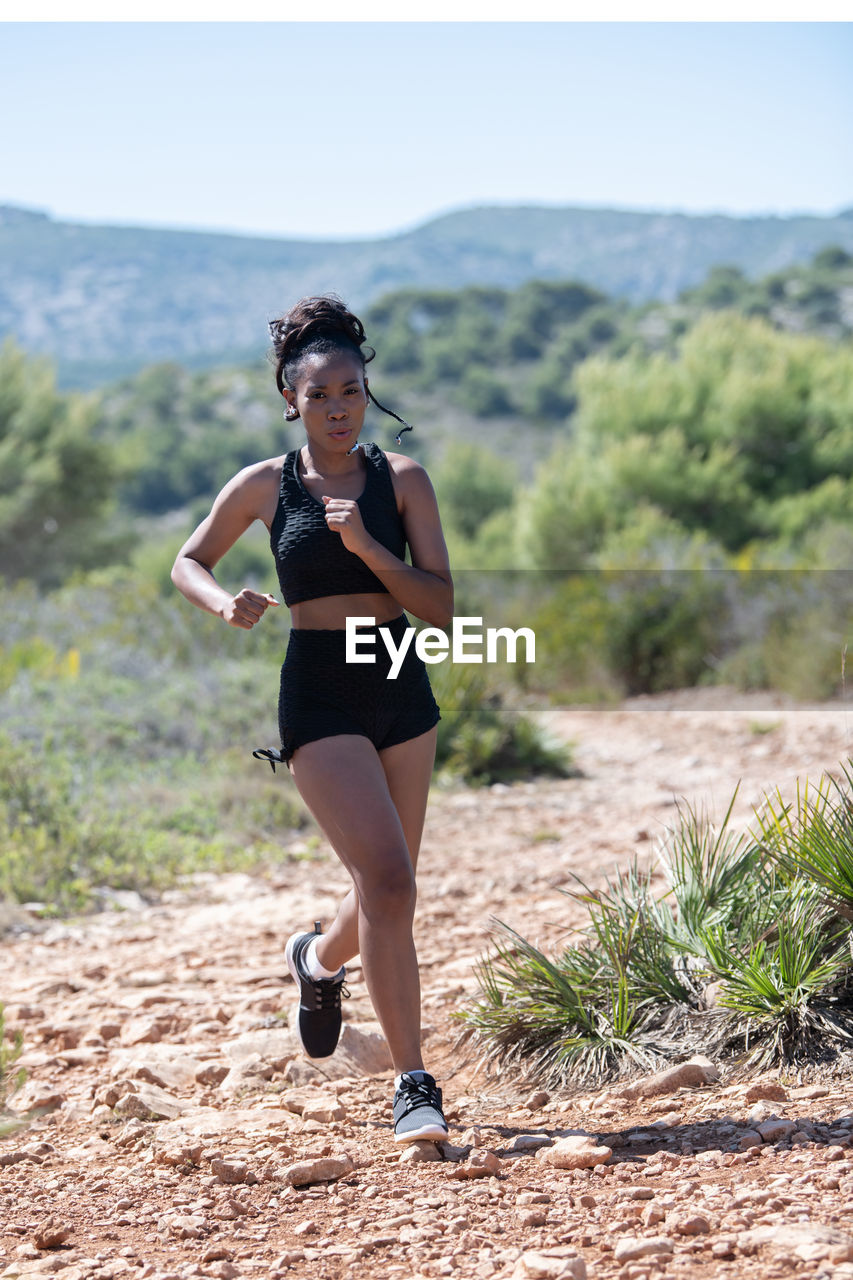 FULL LENGTH PORTRAIT OF YOUNG WOMAN RUNNING ON LAND