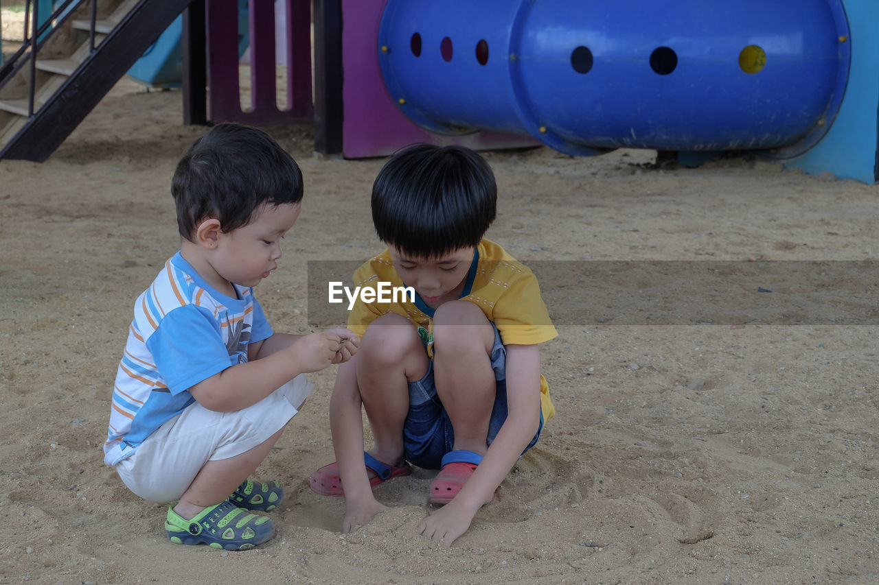 Full length of cute boys playing with sand at playground