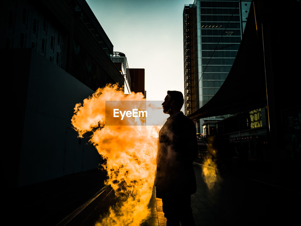 Double exposure of man standing by fire with city in background