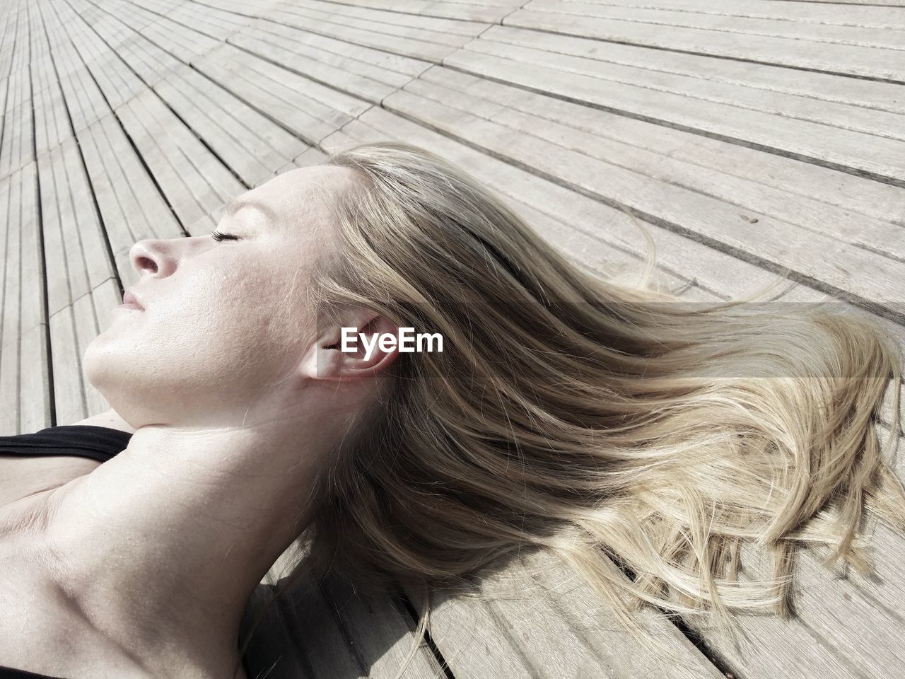 Close-up of young woman lying on boardwalk during sunny day