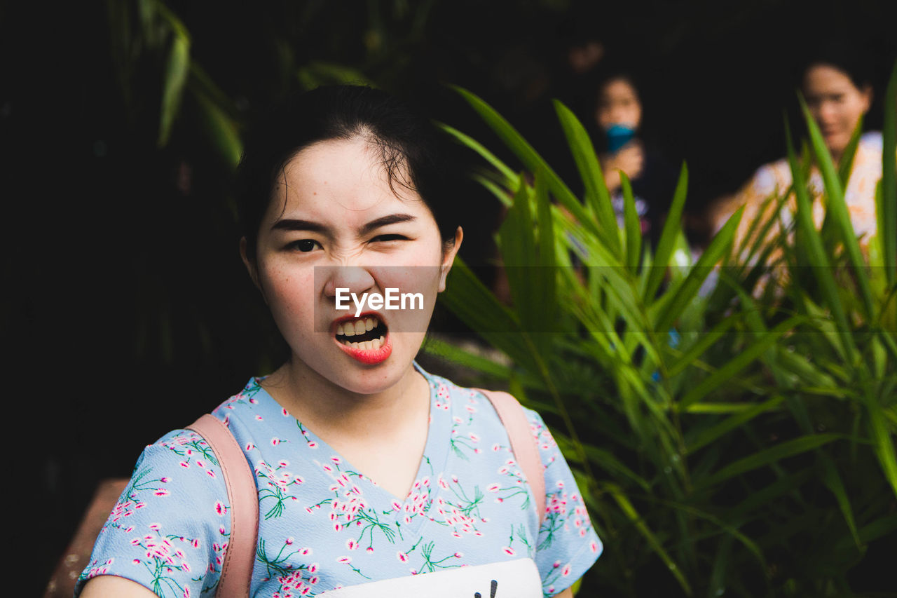 Portrait of smiling young woman making face against plants 