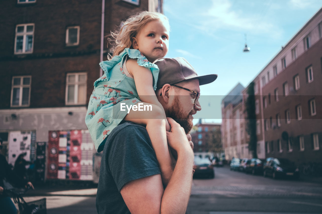 Side view of father carrying daughter on shoulders at city street