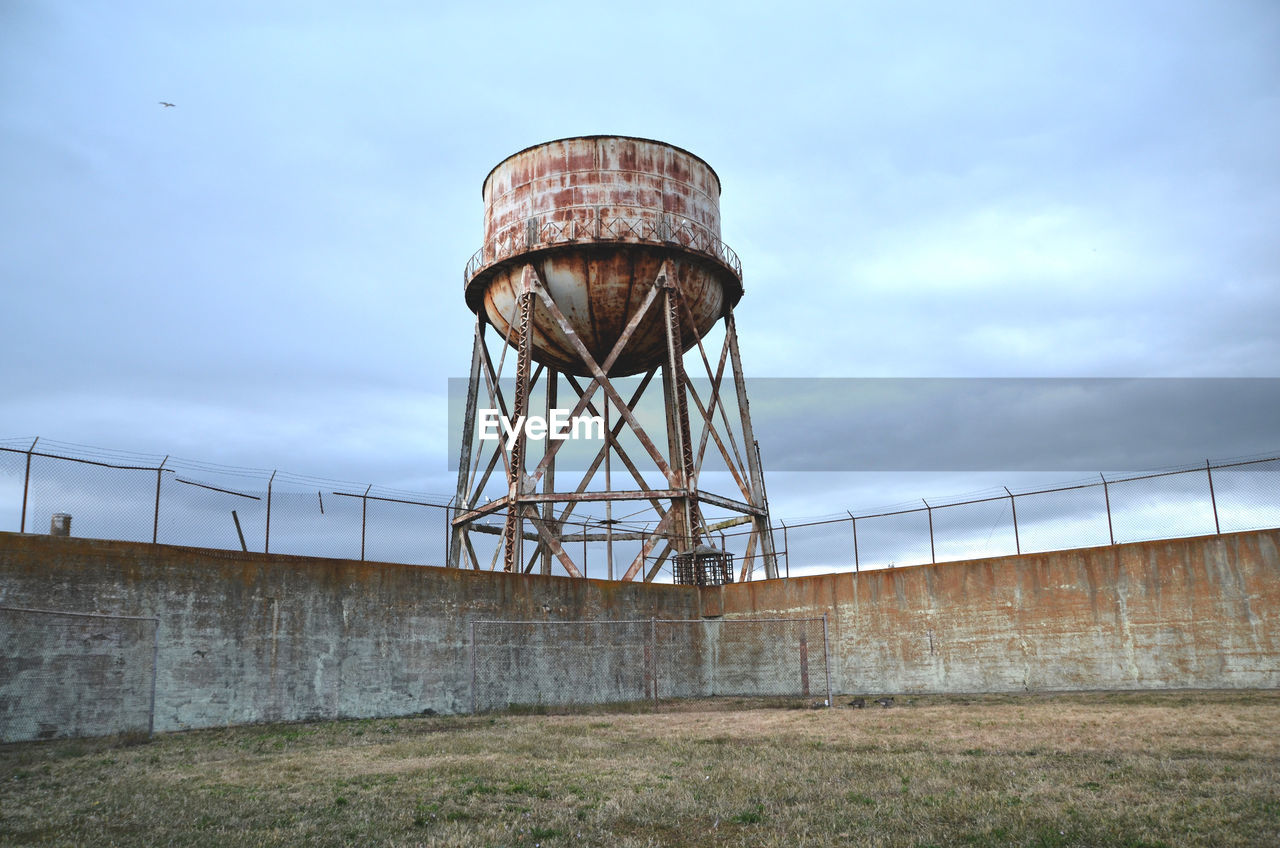 Old rusty metallic water tank by surrounding wall against sky