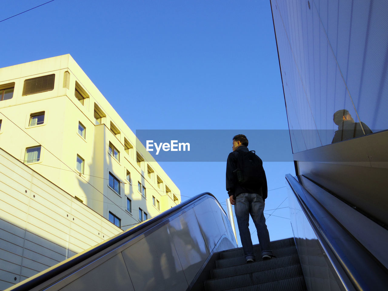 FULL LENGTH REAR VIEW OF MAN STANDING AGAINST BUILDING