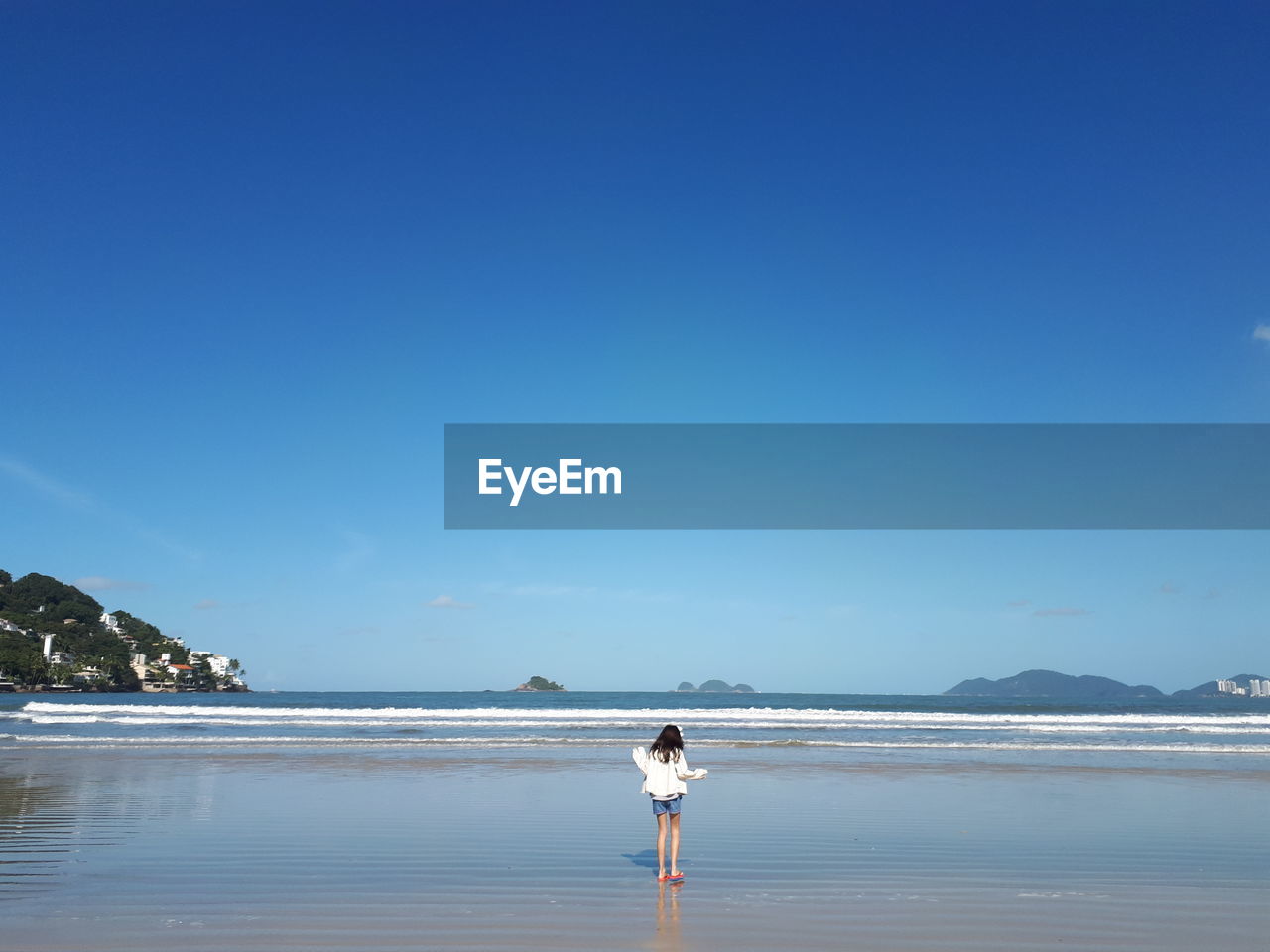 Girl standing at beach against blue sky