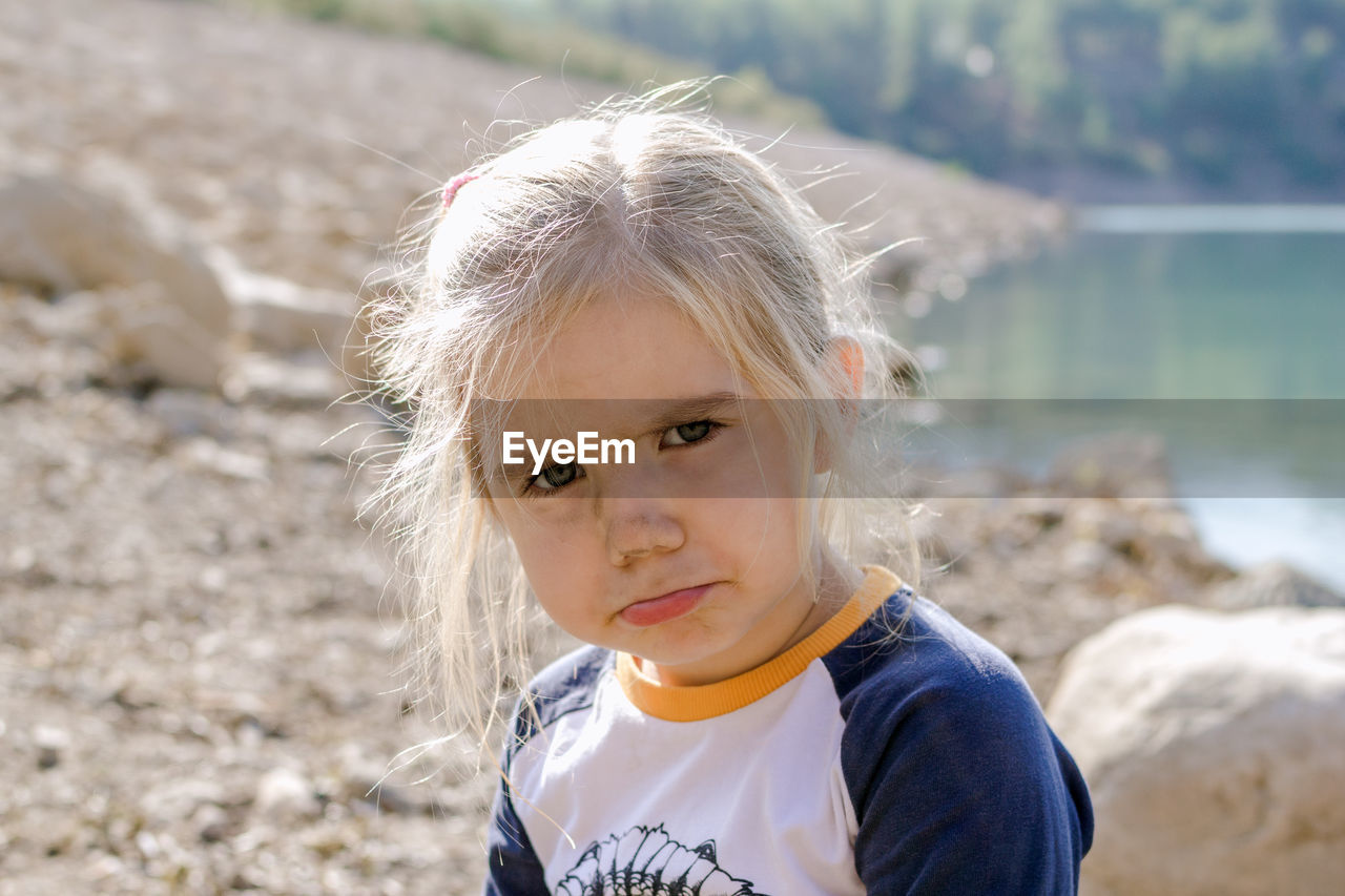 Little girl with blond hair looking at the camera with a sad expression on her face.