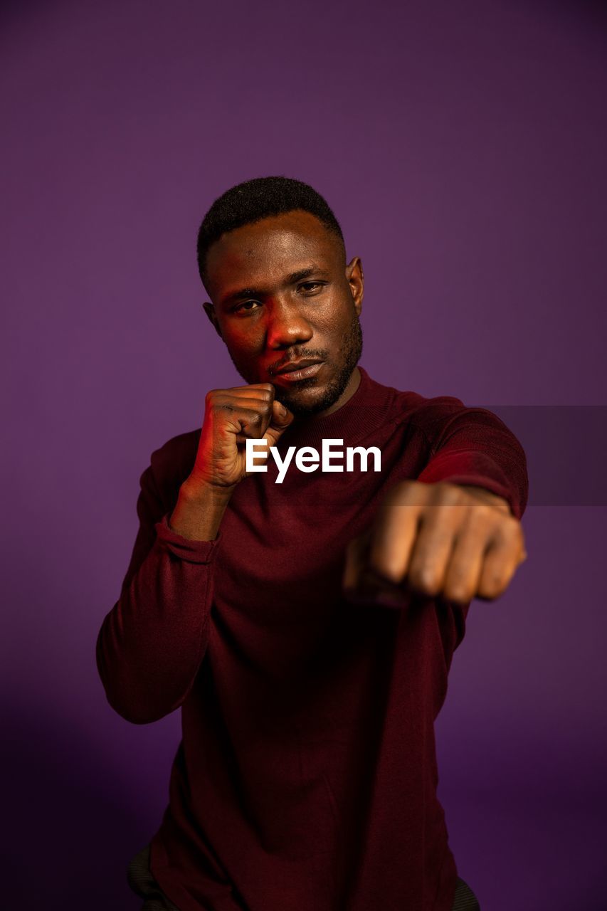 PORTRAIT OF YOUNG MAN STANDING AGAINST COLORED BACKGROUND