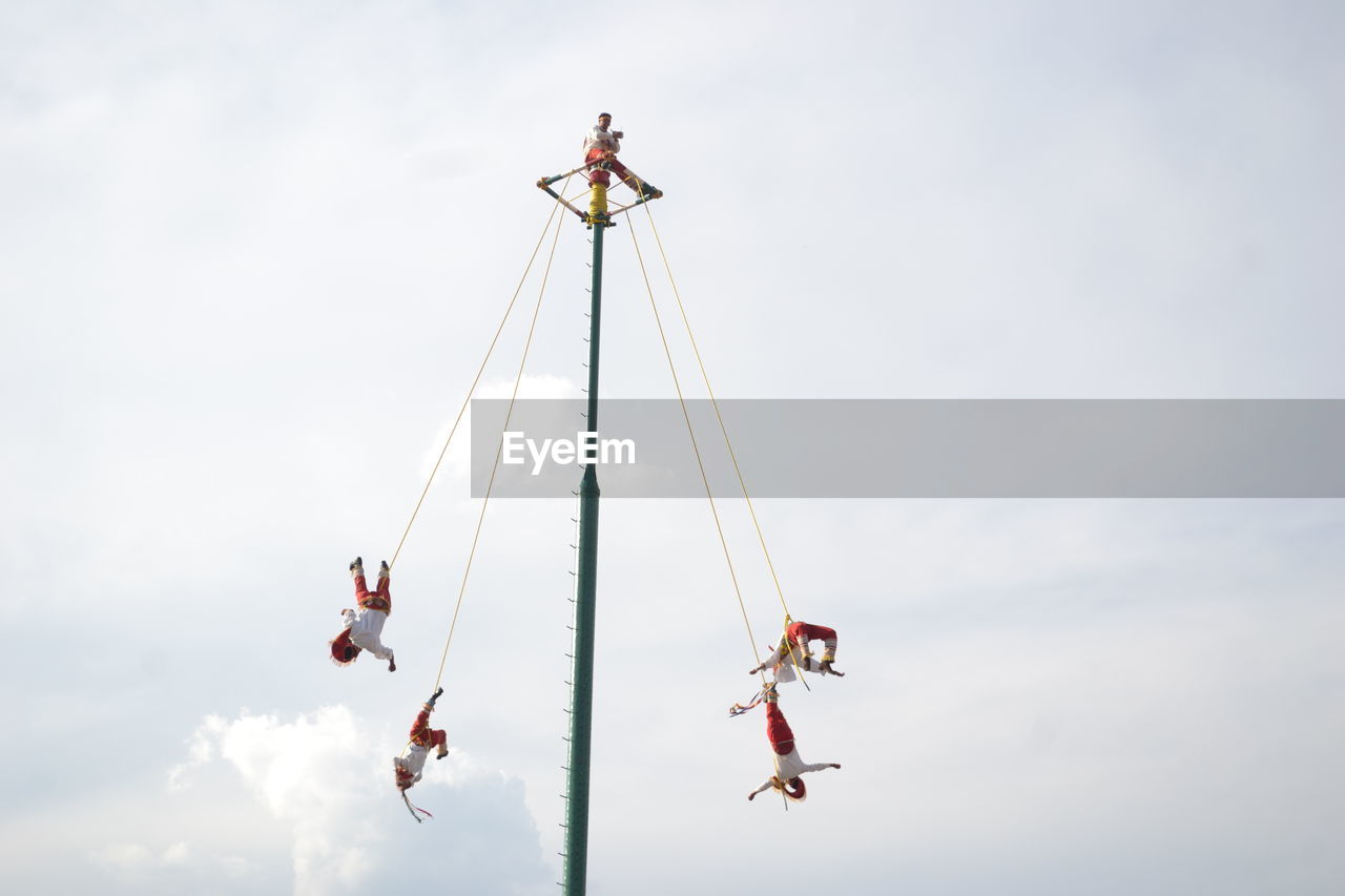 Low angle view of people hanging on ropes against sky