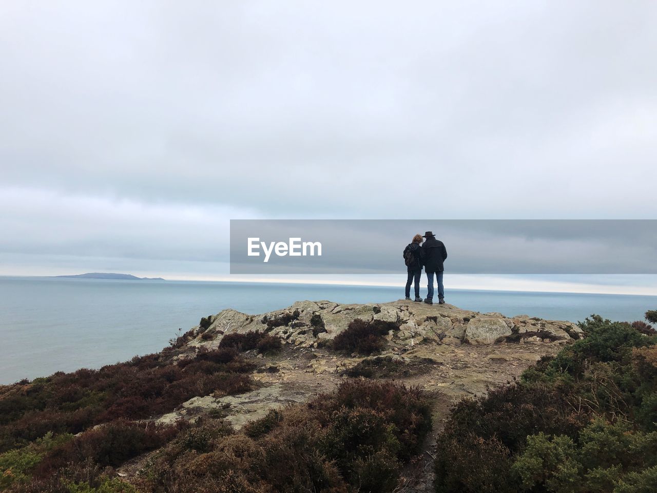 REAR VIEW OF MEN STANDING ON SHORE AGAINST SKY