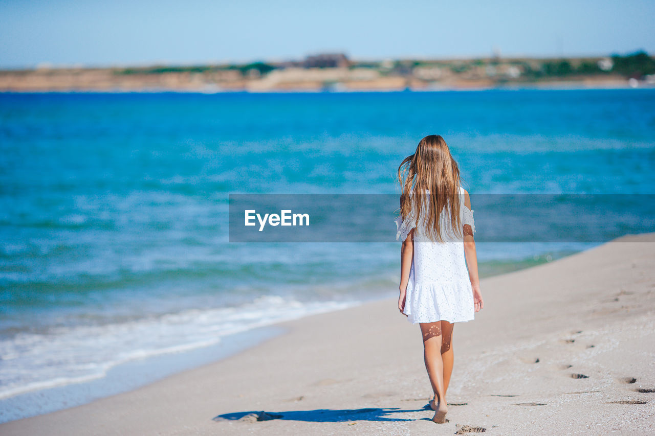 rear view of woman standing at beach against sky