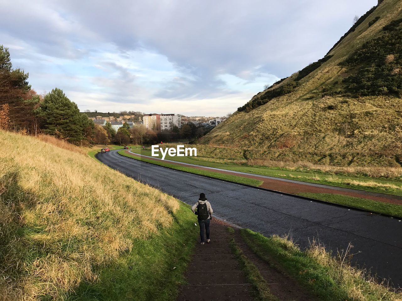 REAR VIEW OF PERSON WALKING ON ROAD BY MOUNTAIN