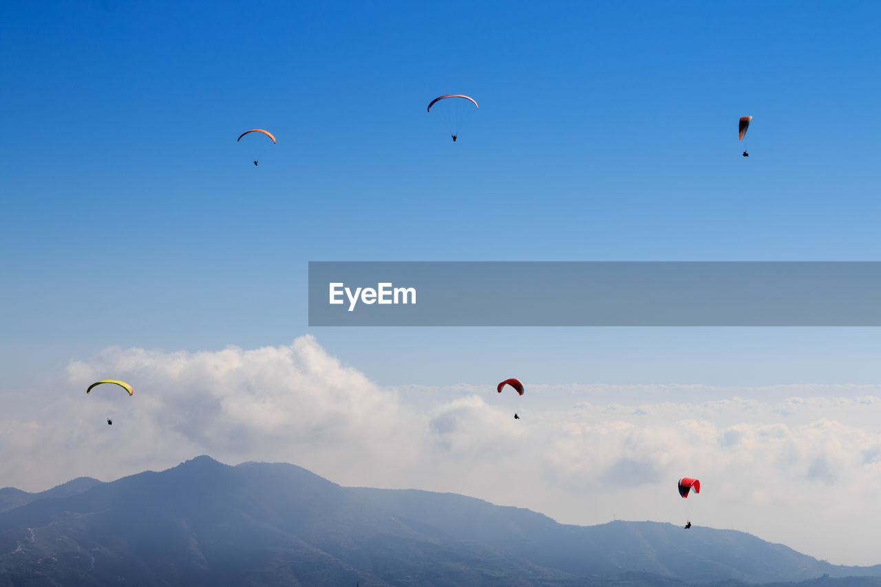 Low angle view of people paragliding against sky