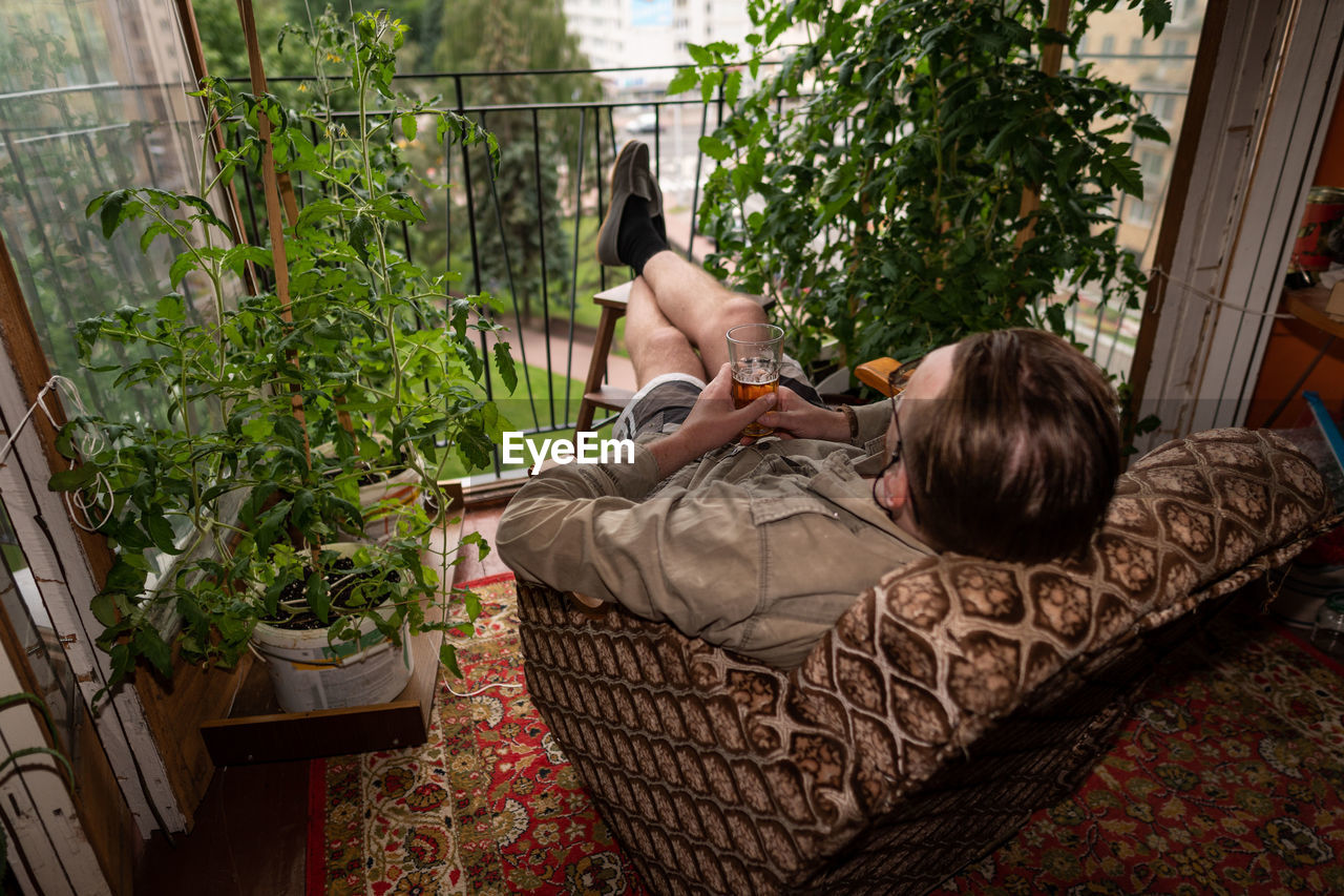 A man resting on a balcony among a home garden.