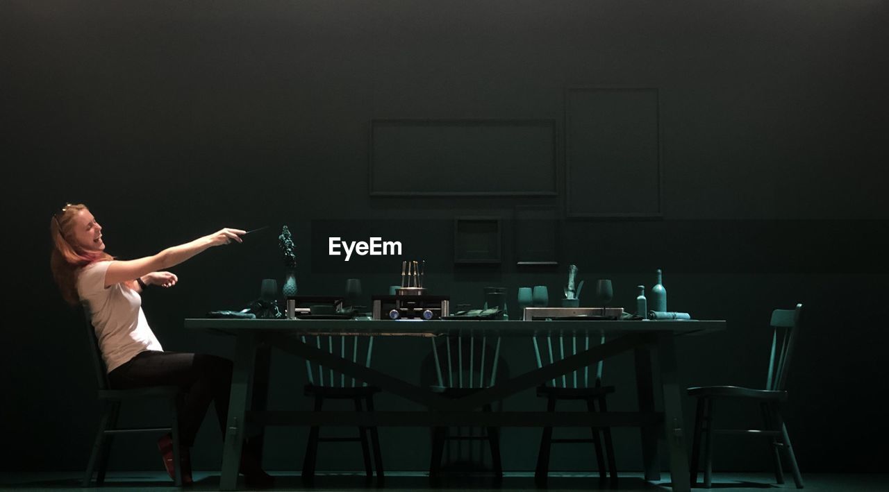 Woman laughing and gesturing while sitting on chair at dining table in darkroom