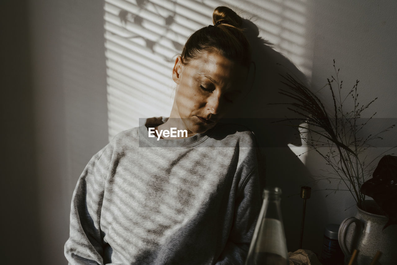 Mature woman with eyes closed against wall at home