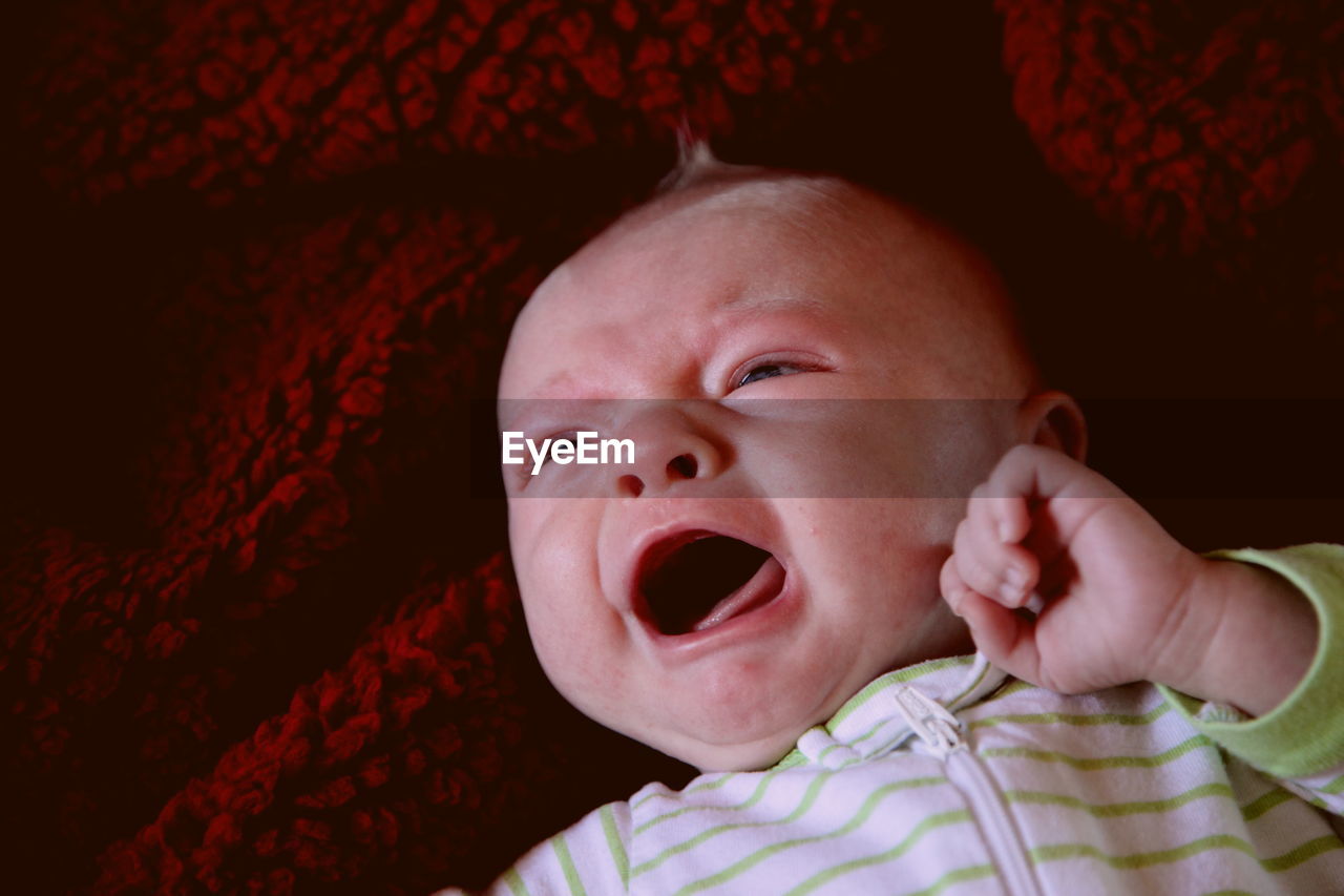 Close-up of cute baby crying while lying on bed