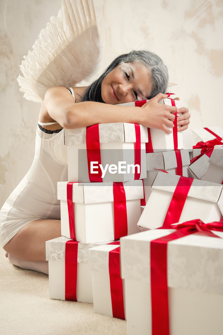 Portrait of female model in angel costume holding christmas presents