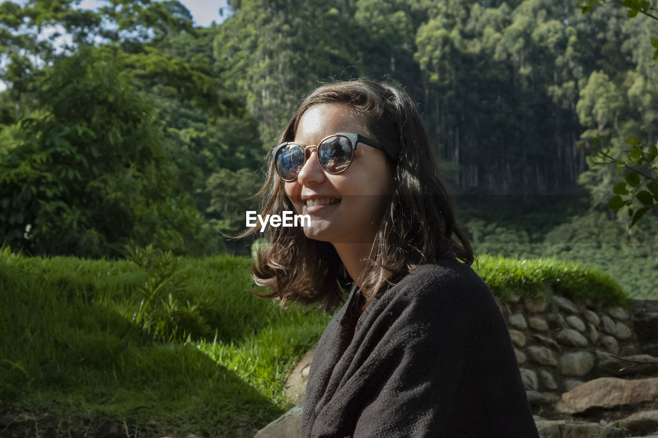 Smiling young woman wearing sunglasses while sitting in park