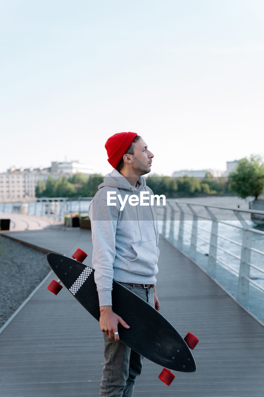 Hipster guy with longboard on city bridge. trendy man hipster skateboarder hold skateboard in hand