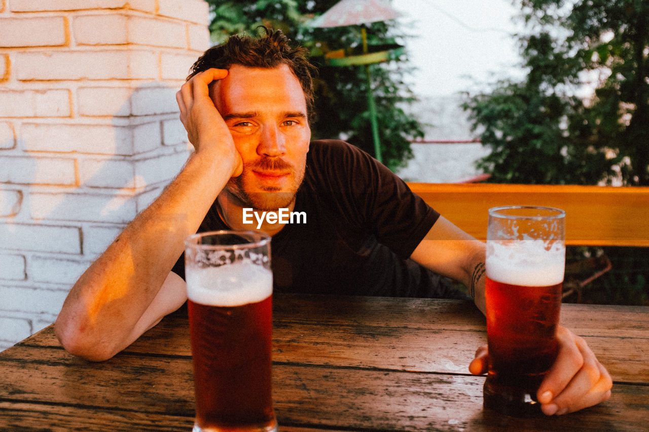 Portrait of man having beer at table during sunset