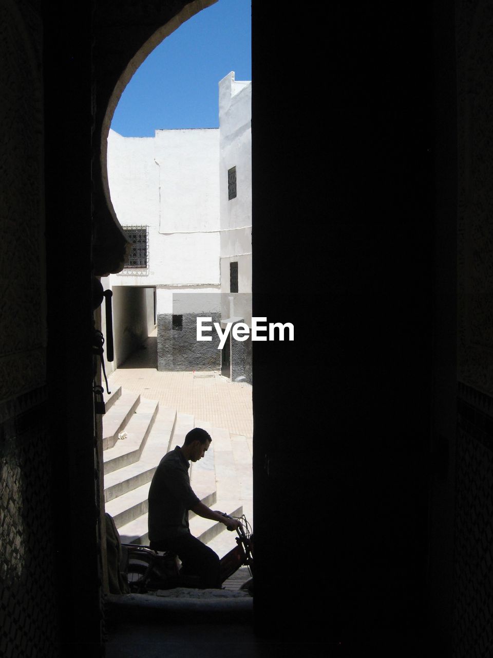 SIDE VIEW OF MAN SITTING AGAINST BUILDINGS